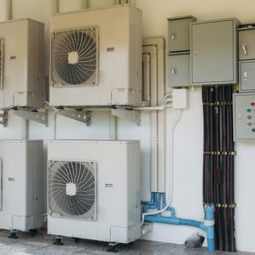 A row of air conditioners are mounted on a wall. The air conditioners are white and have a fan on top